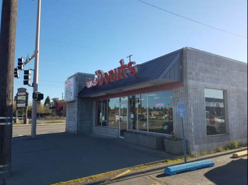 A donut shop with a sign reading "Donut's," featuring large windows and an "Open" sign, on a sunny day.
