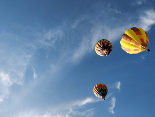 Three colorful hot air balloons float against a bright blue sky with wispy clouds.