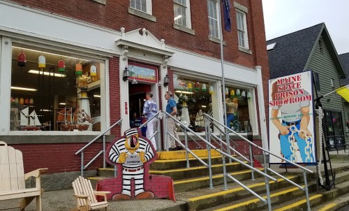 Two people stand outside the Maine State Prison Showroom, featuring colorful decor and a large sign.