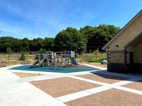 A playground with slides and climbing structures next to a building, surrounded by trees and blue sky.