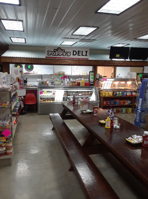 Interior of Poppy's Deli featuring a display case, snack shelves, and a large wooden table. Brightly lit and inviting.