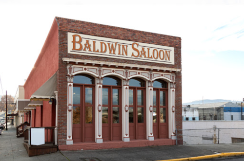 Exterior of Baldwin Saloon, featuring a brick facade and large windows, set in a historic building.