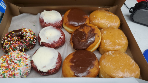 A box of assorted donuts, including frosted, chocolate-covered, and sprinkled varieties.
