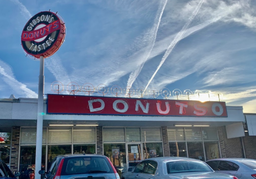 Sign for Gibson's Donuts with a retro design, featuring "DONUTS" in bold letters and a bright sky in the background.