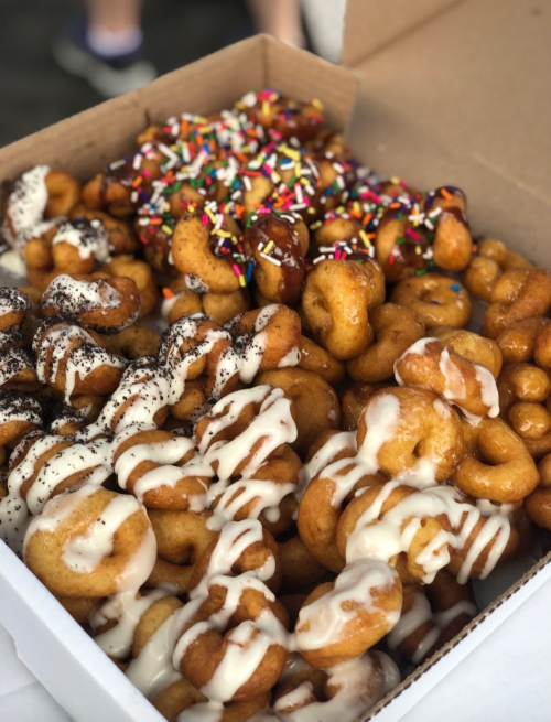 A box filled with assorted mini donuts, topped with icing, sprinkles, and chocolate drizzle.