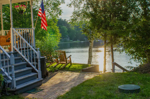 A peaceful lakeside scene with a porch, American flag, and sunlight reflecting on the water.