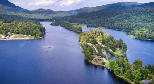 Aerial view of a serene lake surrounded by lush green mountains and a small island with houses.