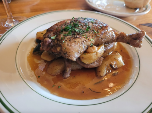 A plated dish featuring roasted chicken leg on a bed of potatoes and vegetables, garnished with herbs.