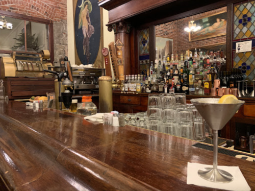 A bar counter with a cocktail glass, bottles on shelves, and a vintage decor backdrop.