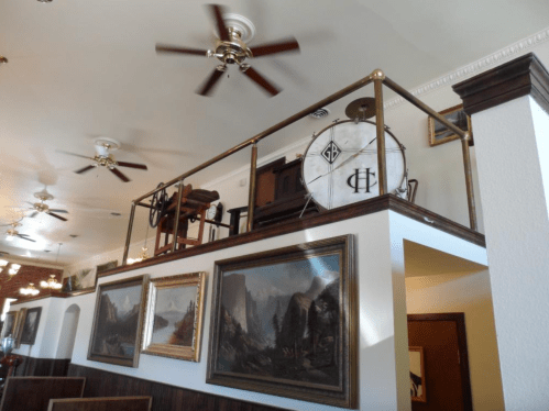 A vintage drum and piano on a balcony, surrounded by framed paintings and ceiling fans in a cozy interior.