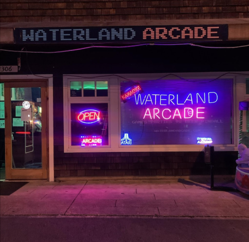 Brightly lit storefront of Waterland Arcade, featuring neon signs and an inviting "OPEN" display.