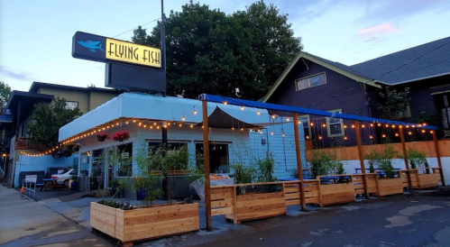 Exterior of Flying Fish restaurant with a blue sign, outdoor seating, and string lights in a cozy neighborhood setting.