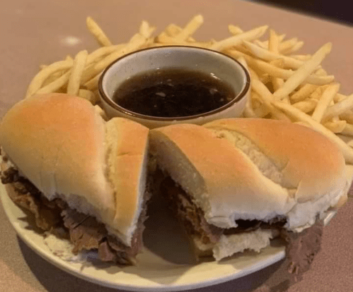 A plate with two halves of a beef sandwich, served with fries and a small bowl of dipping sauce.