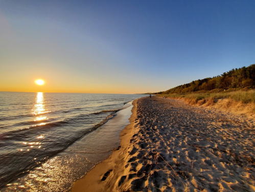 A serene beach at sunset, with gentle waves lapping at the shore and a golden sun reflecting on the water.