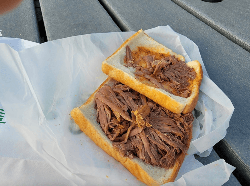 A sandwich with two slices of bread filled with shredded beef, resting on a piece of white paper on a wooden table.