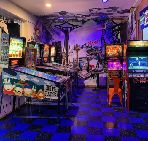 A vibrant arcade room with pinball machines and classic arcade games, featuring colorful murals and checkered flooring.