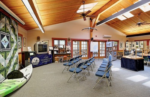 Interior of a community center with chairs arranged for an event, featuring a kayak, displays, and large windows.