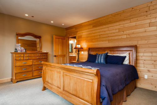 Cozy bedroom with wooden walls, a large bed, dresser, and warm lighting.