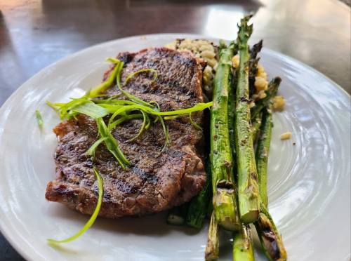 A plate featuring a grilled steak with green onions, served alongside asparagus and a portion of rice.