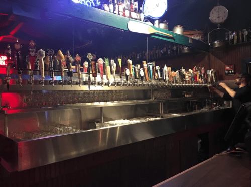 A bar with a long row of beer taps and a bartender preparing drinks in a dimly lit setting.