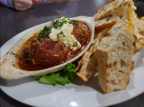 A dish of meatballs in marinara sauce topped with cheese and herbs, served with slices of toasted bread on the side.