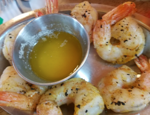 A plate of grilled shrimp with a small bowl of melted butter for dipping.