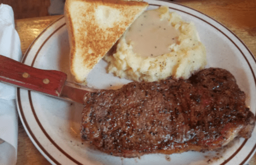 A plate with a grilled steak, mashed potatoes with gravy, and a slice of toasted bread.