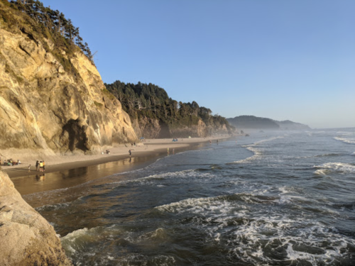 A serene beach scene with gentle waves, cliffs, and people enjoying the shoreline under a clear blue sky.