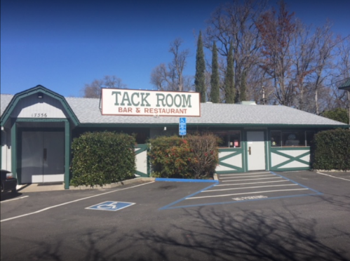 Exterior of the Tack Room Bar & Restaurant, featuring a sign and accessible parking spaces. Trees in the background.