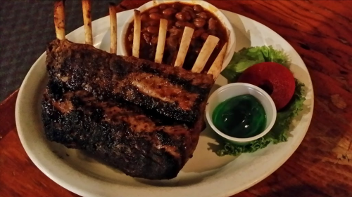 A plate featuring grilled ribs, baked beans, a green gelatin dessert, and a slice of tomato on lettuce.