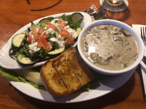 A plate with a fresh salad, creamy soup, and toasted bread, served on a wooden table.