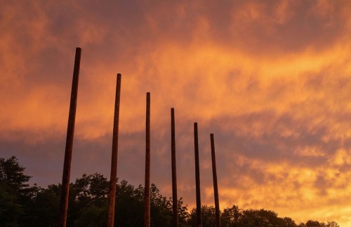 Silhouetted poles against a vibrant orange and purple sunset sky, with trees in the background.