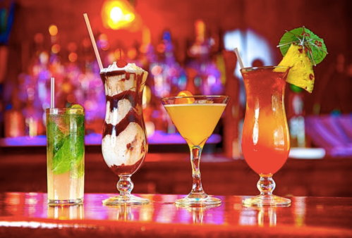 Four colorful cocktails on a bar, featuring a mojito, sundae drink, martini, and tropical punch, with a vibrant background.