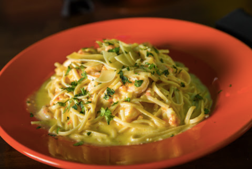 A vibrant orange plate filled with creamy pasta topped with shrimp and garnished with fresh herbs.