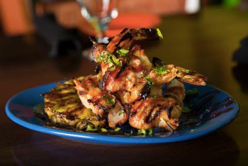Grilled shrimp skewers on a blue plate, garnished with herbs, served with grilled pineapple slices.