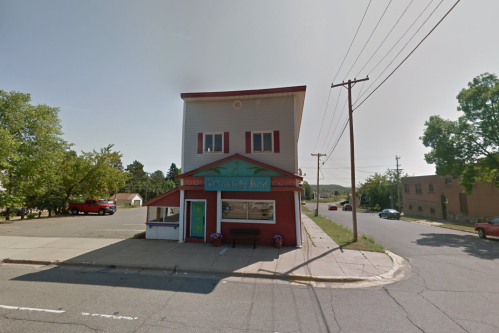 A colorful two-story building with a sign reading "Whistling Bird," located on a quiet street with trees and parked cars.