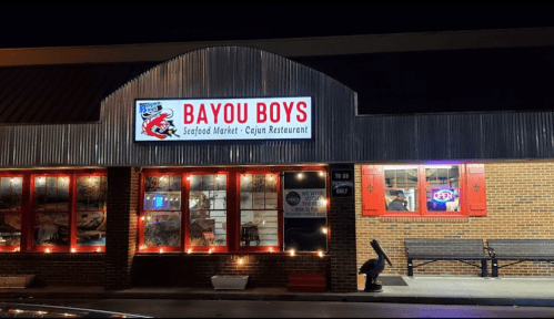 Exterior of Bayou Boys Seafood Market and Cajun Restaurant, featuring a lit sign and red window shutters at night.