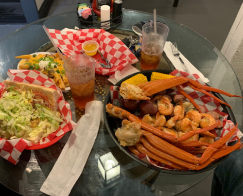 A table with seafood, crab legs, shrimp, corn, and drinks, served on checkered paper plates.