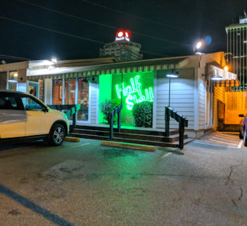 A nighttime view of a restaurant with a green neon sign reading "Half Shell" and parked cars in front.