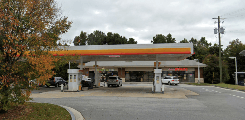 A gas station with a convenience store, featuring multiple pumps and a cloudy sky in the background.