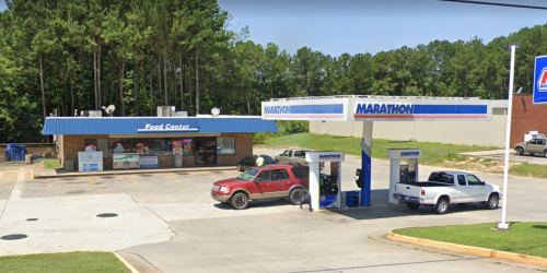 A Marathon gas station and convenience store surrounded by trees, with vehicles at the pumps and a blue awning.