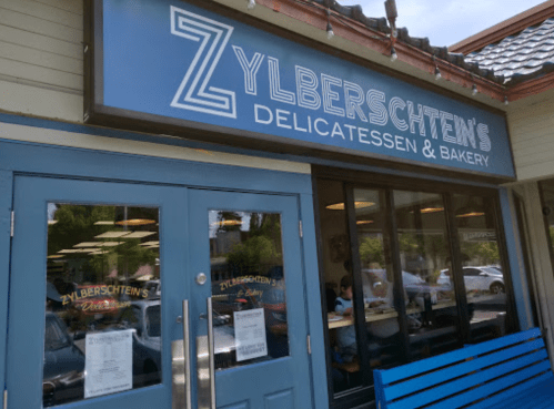 Exterior of Zylberschten's Delicatessen & Bakery, featuring a blue door and large windows with diners inside.