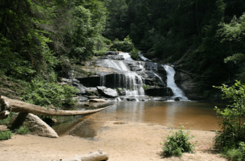 A serene waterfall cascades over rocks into a calm pool, surrounded by lush greenery and trees.