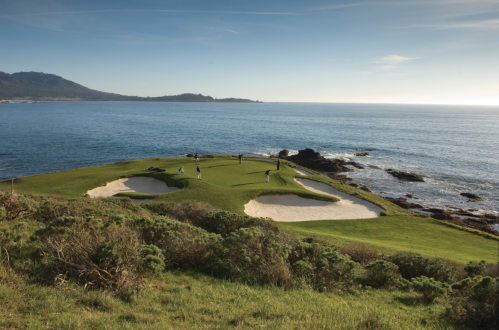 A scenic golf course overlooking the ocean, with players on the green and sandy bunkers nearby.