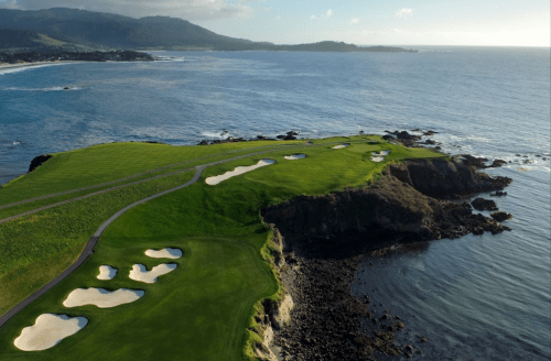 Aerial view of a coastal golf course with sandy bunkers and ocean waves in the background.