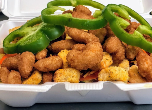 A takeout container filled with crispy chicken pieces, croutons, and green bell pepper slices on top.