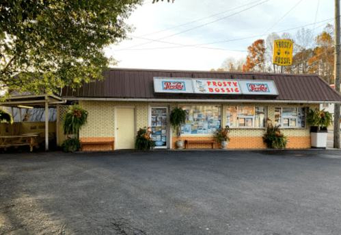 A quaint roadside eatery with a sign reading "Frosty Bossic," surrounded by greenery and autumn foliage.