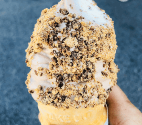 A hand holding a large ice cream cone topped with chocolate soft serve and crushed cookie crumbs.