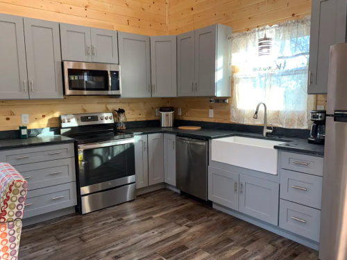 Modern kitchen with gray cabinets, stainless steel appliances, and a farmhouse sink, featuring wooden walls and a cozy atmosphere.
