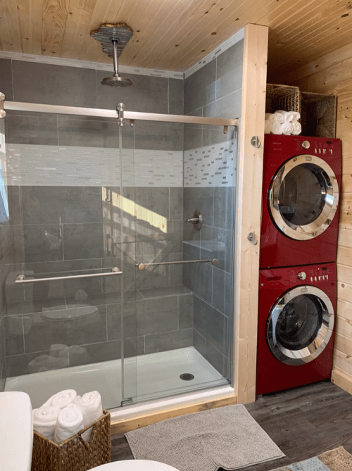 A modern bathroom featuring a glass shower, gray tiles, and a stacked red washer and dryer unit.